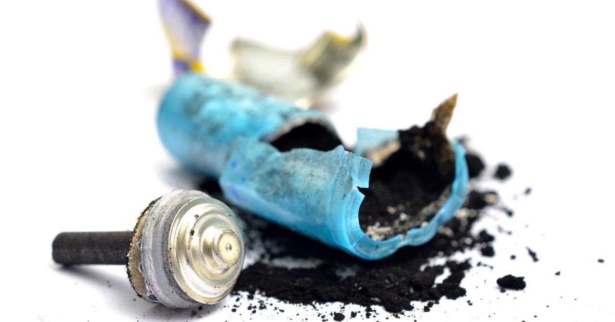 A smashed battery with the metallic top on the left side and black graphite powder spread all around it.